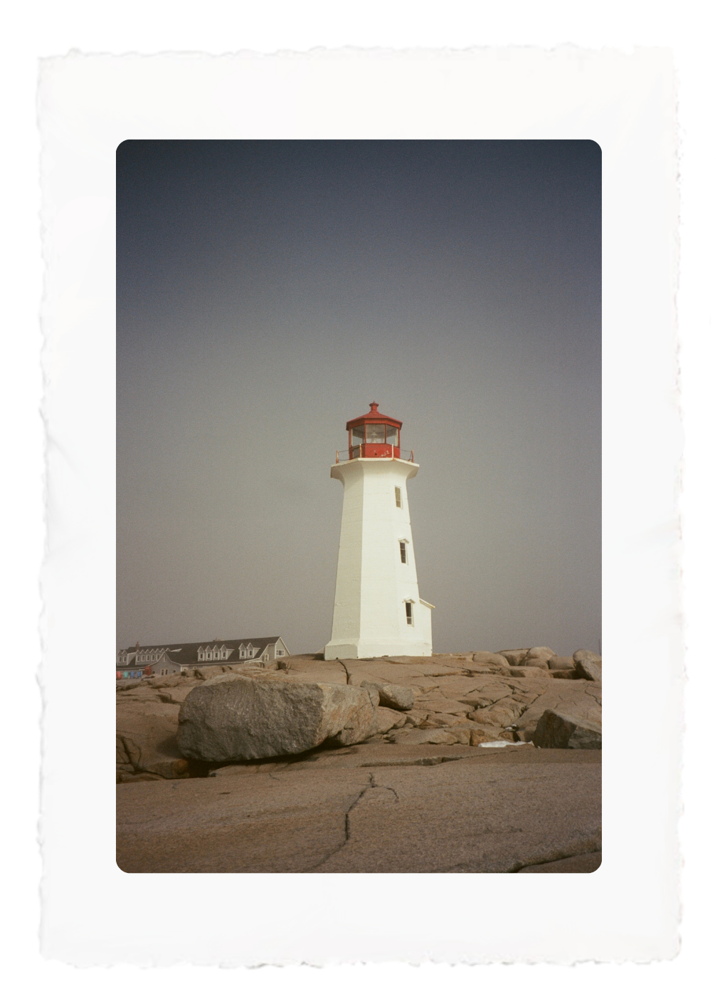 Lighthouse on a rocky shore under a gray sky, framed by a white border.