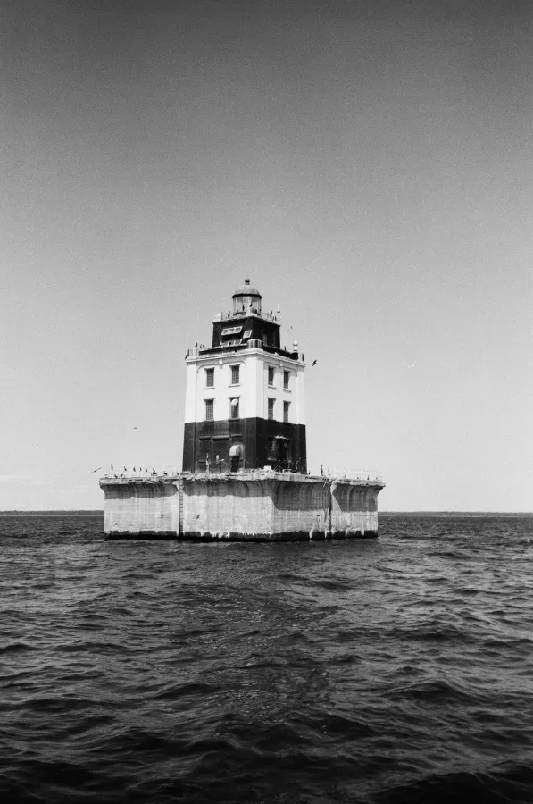 Black and white photo of Poe Reef lighthouse in the middle of a body of water under a clear sky.