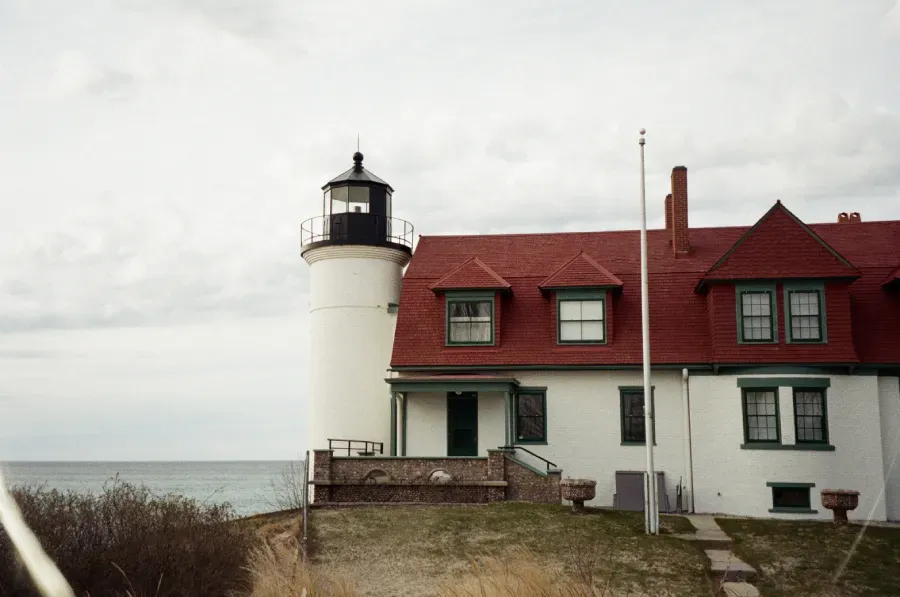 Point Betsie lighthouse next to a white house with a red roof on a cloudy day overlooking the sea.