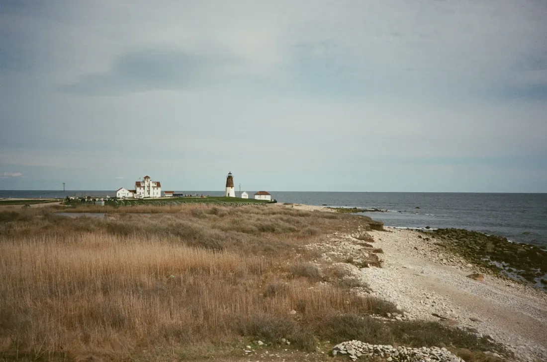 A landscape film photograph of Point Judith lighthouse in the distance of a shoreline