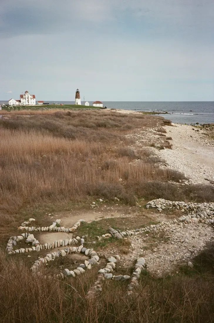 Film photo of a shoreline with rocks spelling the word HOPE and the Point Judith lighthouse in the distance