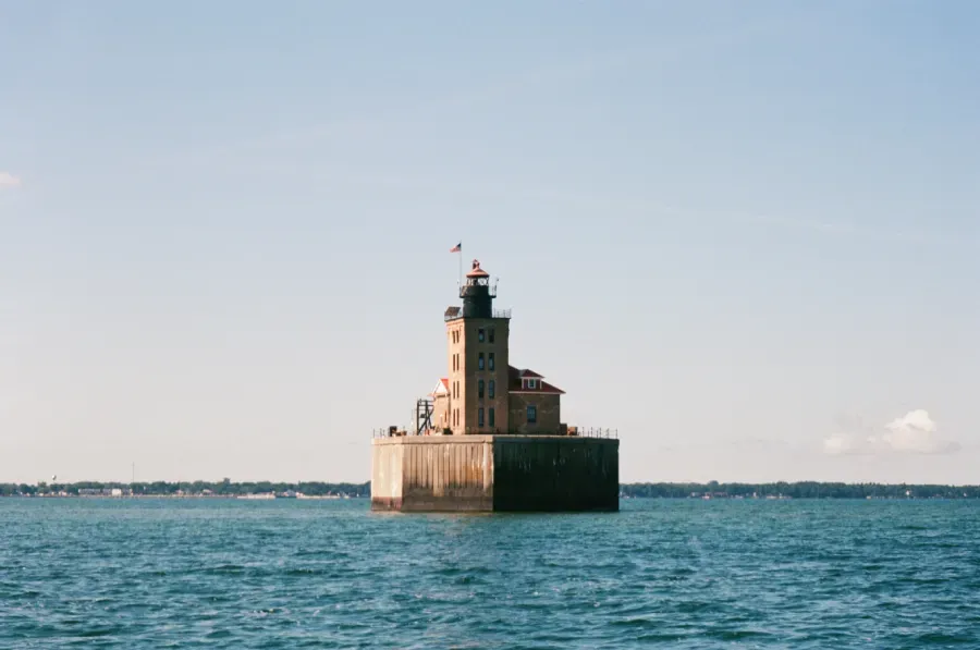 Port Austin Lighthouse on a square stone foundation in the ocean, under a clear blue sky.