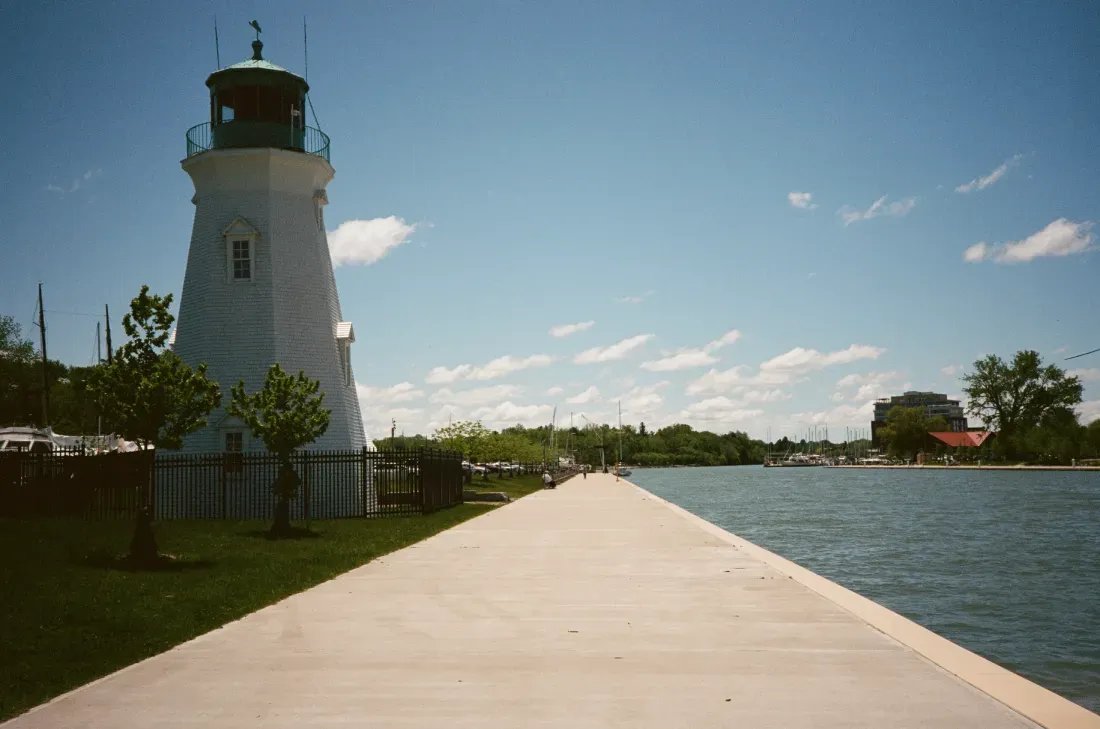 Port Dalhousie lighthouse beside a wide boardwalk and calm water under a blue sky