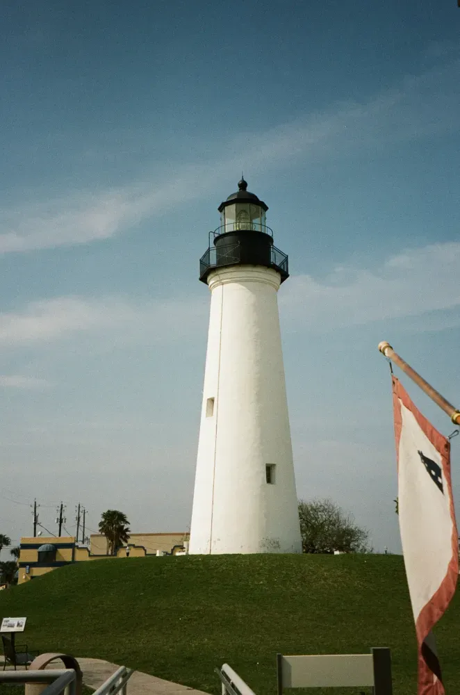 Port Isabel lighthouse on green hill under blue sky, flag in foreground.