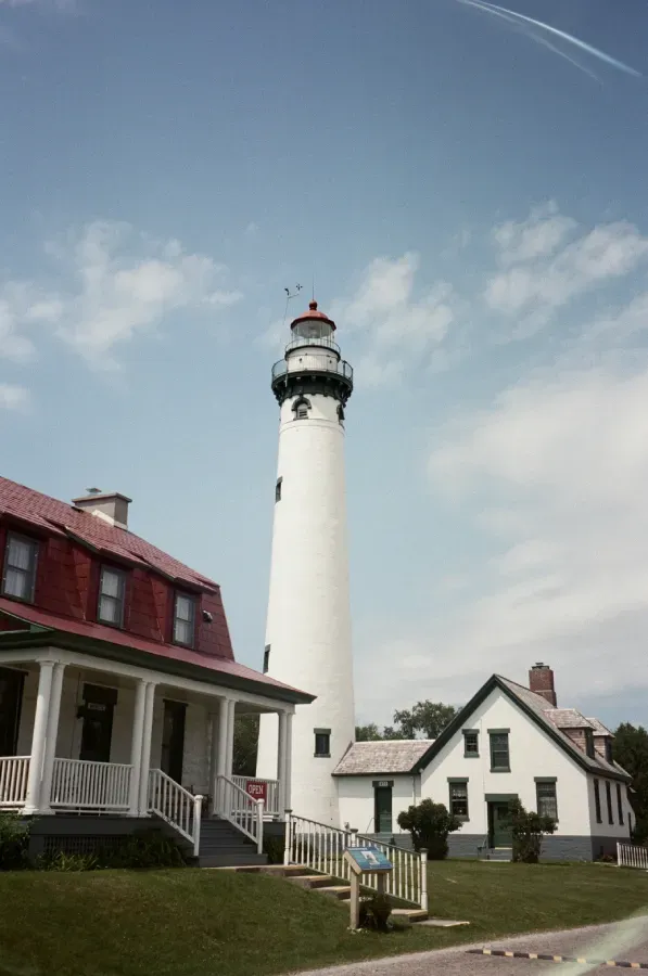 White lighthouse and buildings with red roof under a blue sky.
