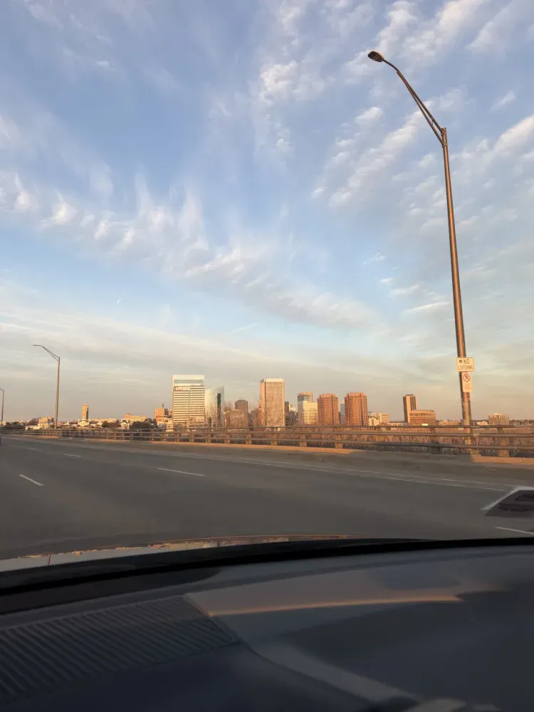 City skyline at sunset seen from a highway, with a curved streetlight and car dashboard in the foreground