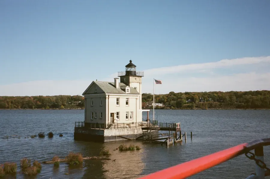 Rondout Creek lighthouse building on a water-covered structure, with a blue sky and American flag.