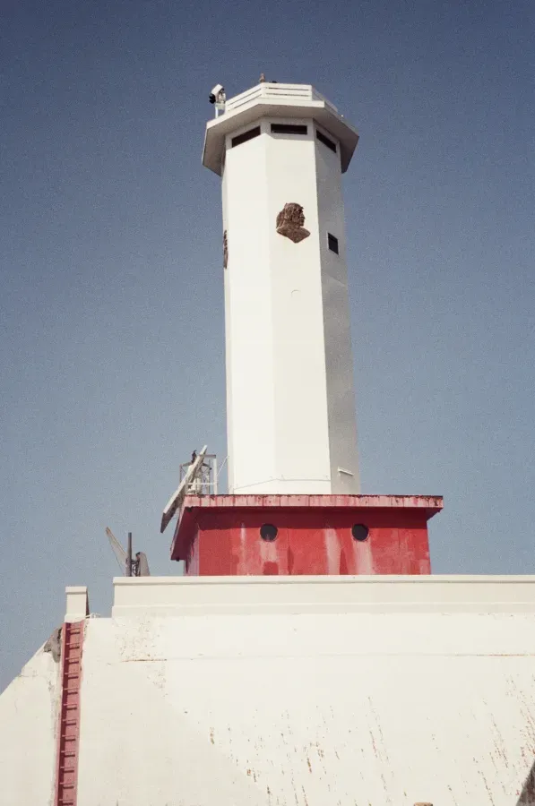 Film photo of Round Island lighthouse tower with red base, under a blue sky.