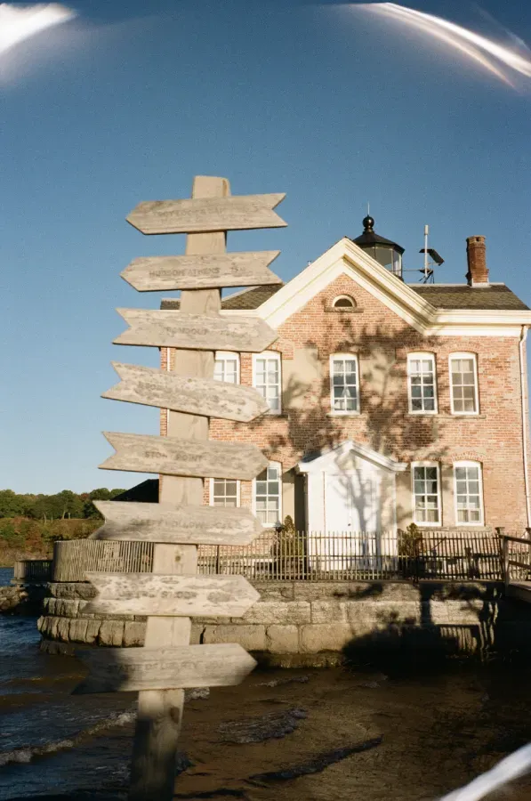 The Saugerties brick lighthouse with multiple wooden directional signs against a blue sky.