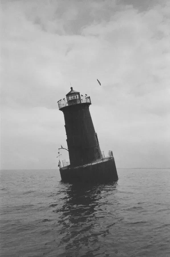 Sharps Island lighthouse in dark water under cloudy sky. Black and white film photograph