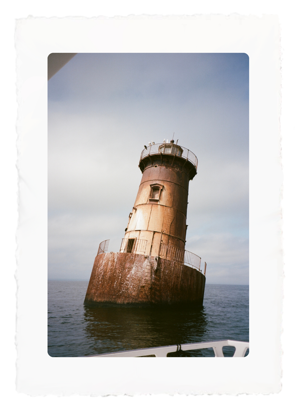 Rusty lighthouse leaning in the sea under a pale sky