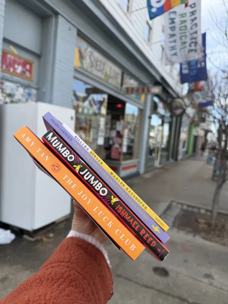 Hand holding 4 books on the street outside of a local book store