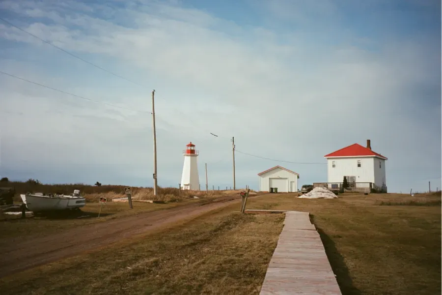 Shipwreck Point lighthouse and a larger white house with a red roof under a cloudy sky