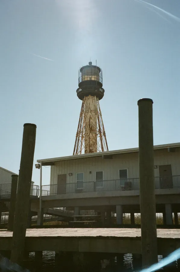 South Pass Lighthouse with yellow metal structure atop a white building on stilts, under a blue sky.