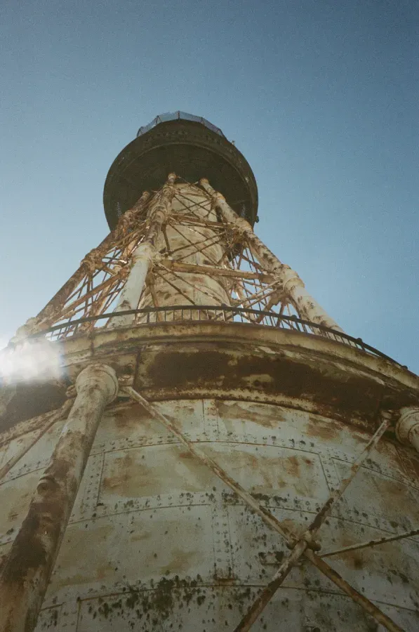 Rusty, metal South Pass Monolith lighthouse against a clear blue sky.