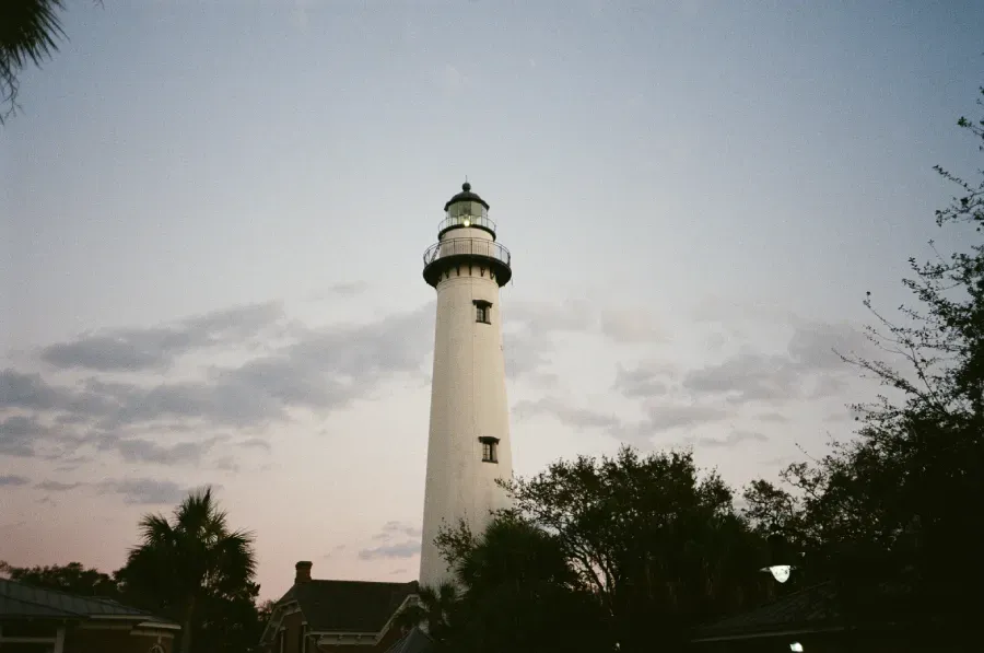 St. Simons Island lighthouse against a cloudy, dusky sky, trees frame the edges.