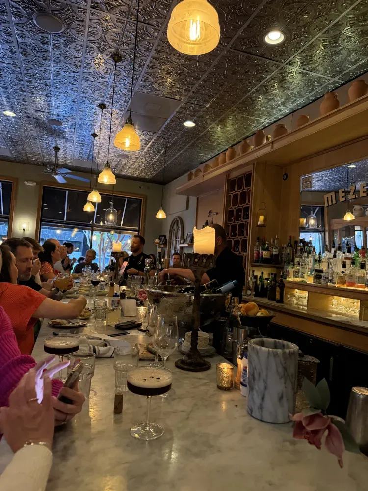 Busy bar with hanging pendant lights, and a marble counter with dishes and drinks