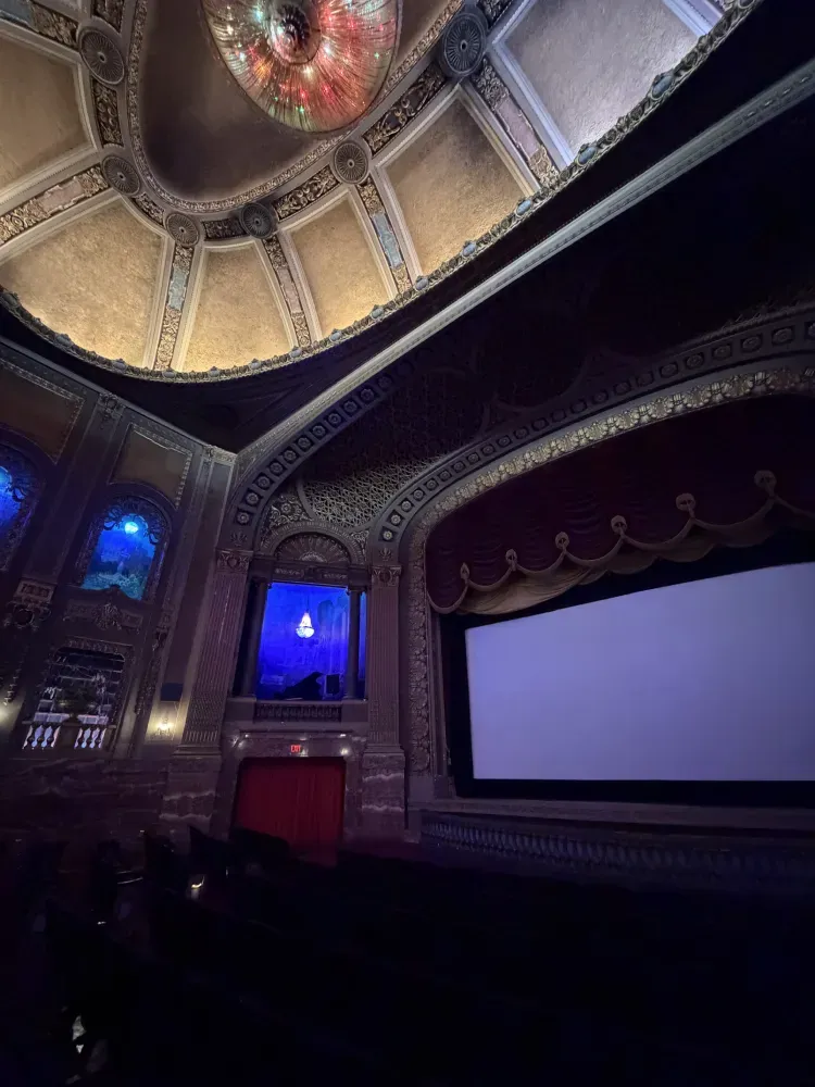 A theater interior with a large screen, blue-lit walls, and decorative ceiling details