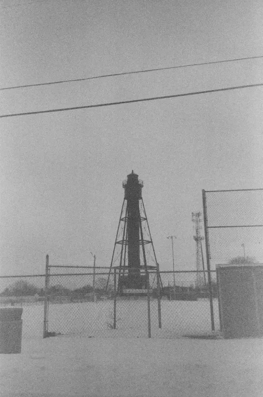 Tinicum Rear Range lighthouse stands in a flat, sandy, fenced-in area under an overcast sky