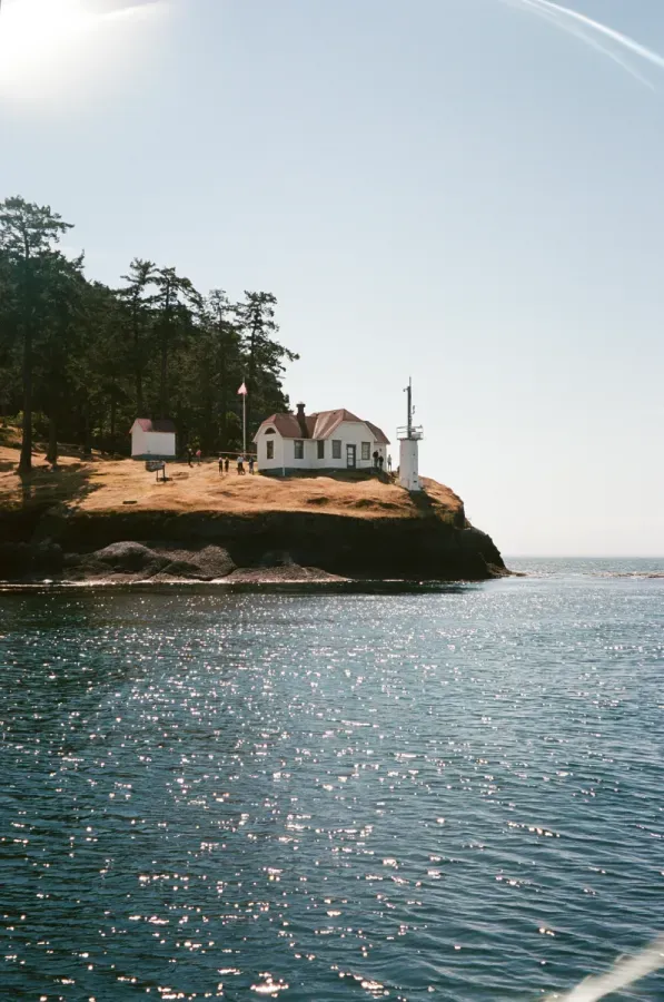 Turn Point Lighthouse on a cliff overlooking the ocean on a sunny day. White building with red roof, blue water.