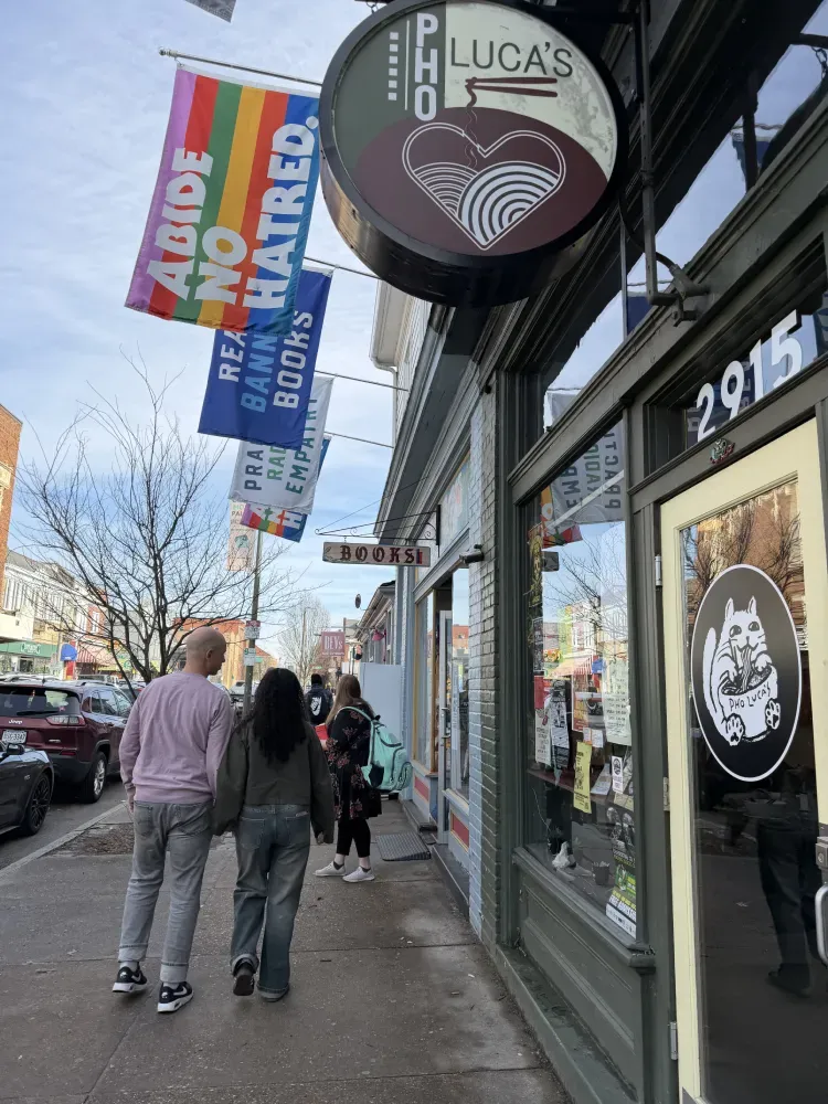 People walking past Pho Lucas storefront signs on a city sidewalk in daylight