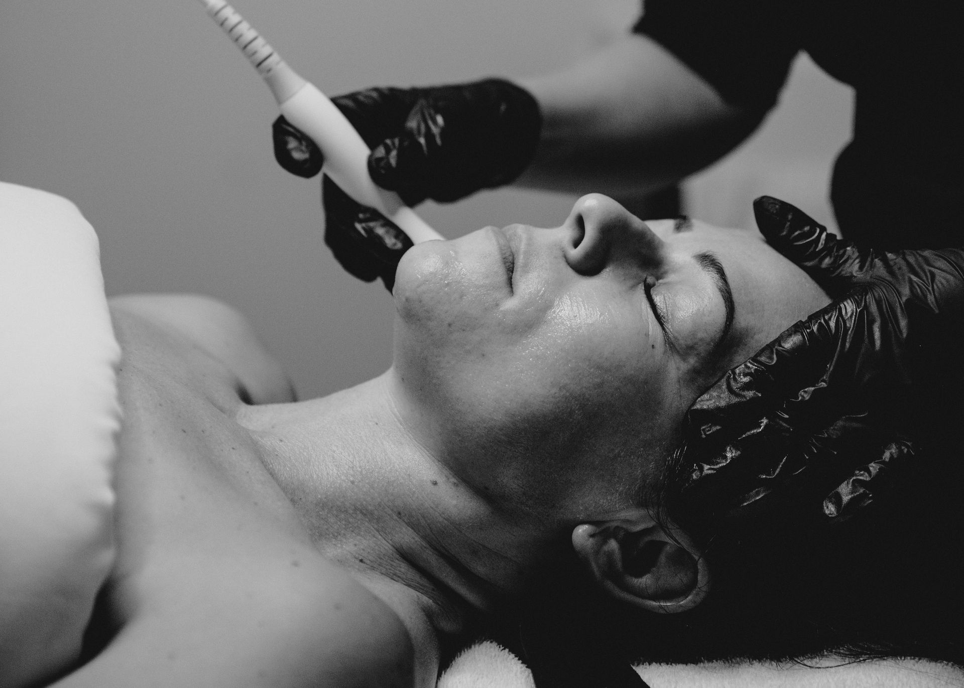 A woman is getting a facial treatment in a black and white photo.