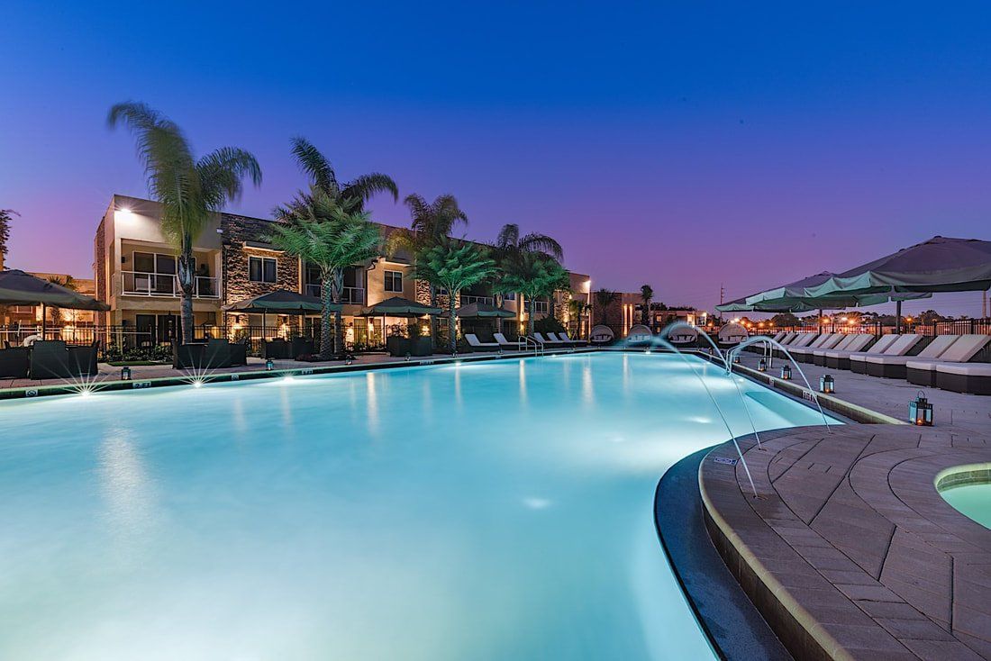 Resort-style pool at night with blue lighting, lounge seating, and landscaped edges.