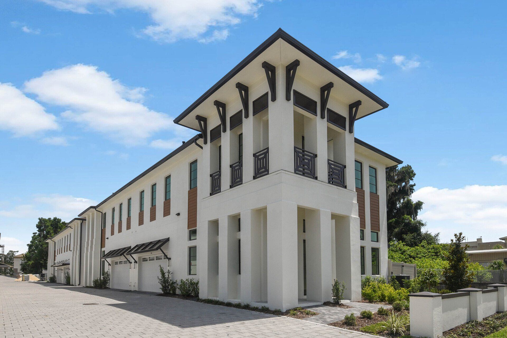 Front view of white luxury townhomes with balconies and manicured landscaping.
