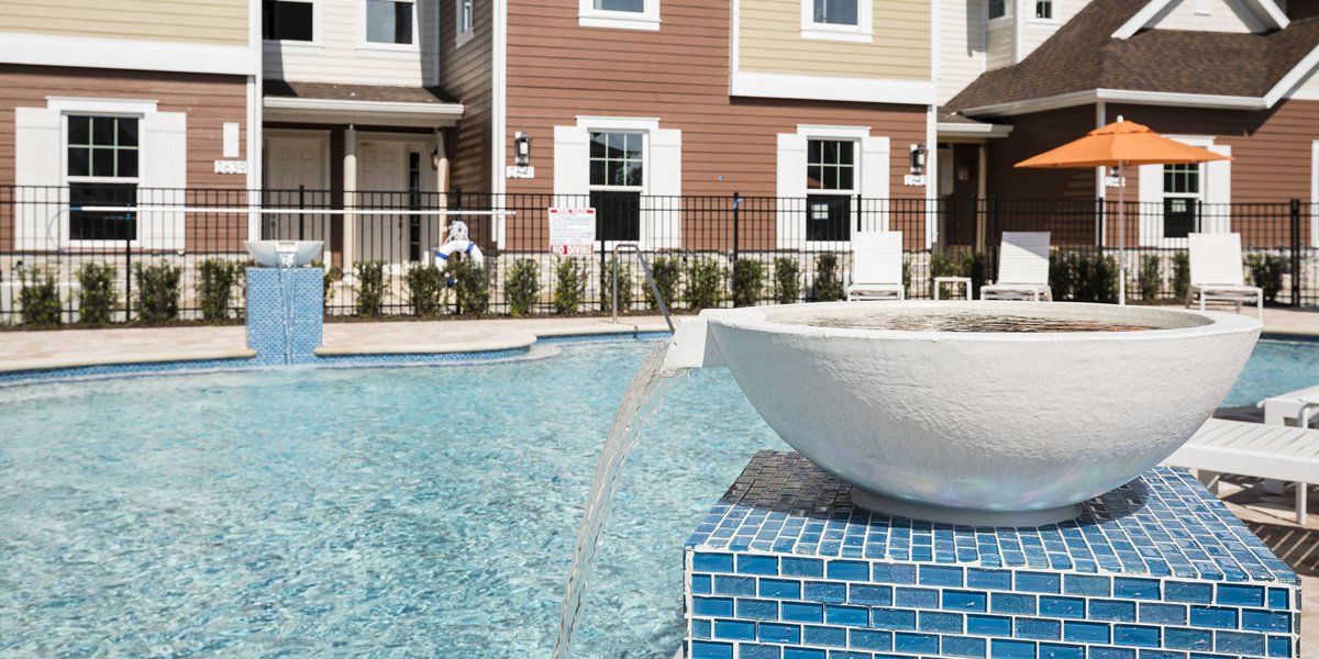 Resort-style pool at Summerville Resort with fountains, patio seating, and multi-story townhomes in the background.