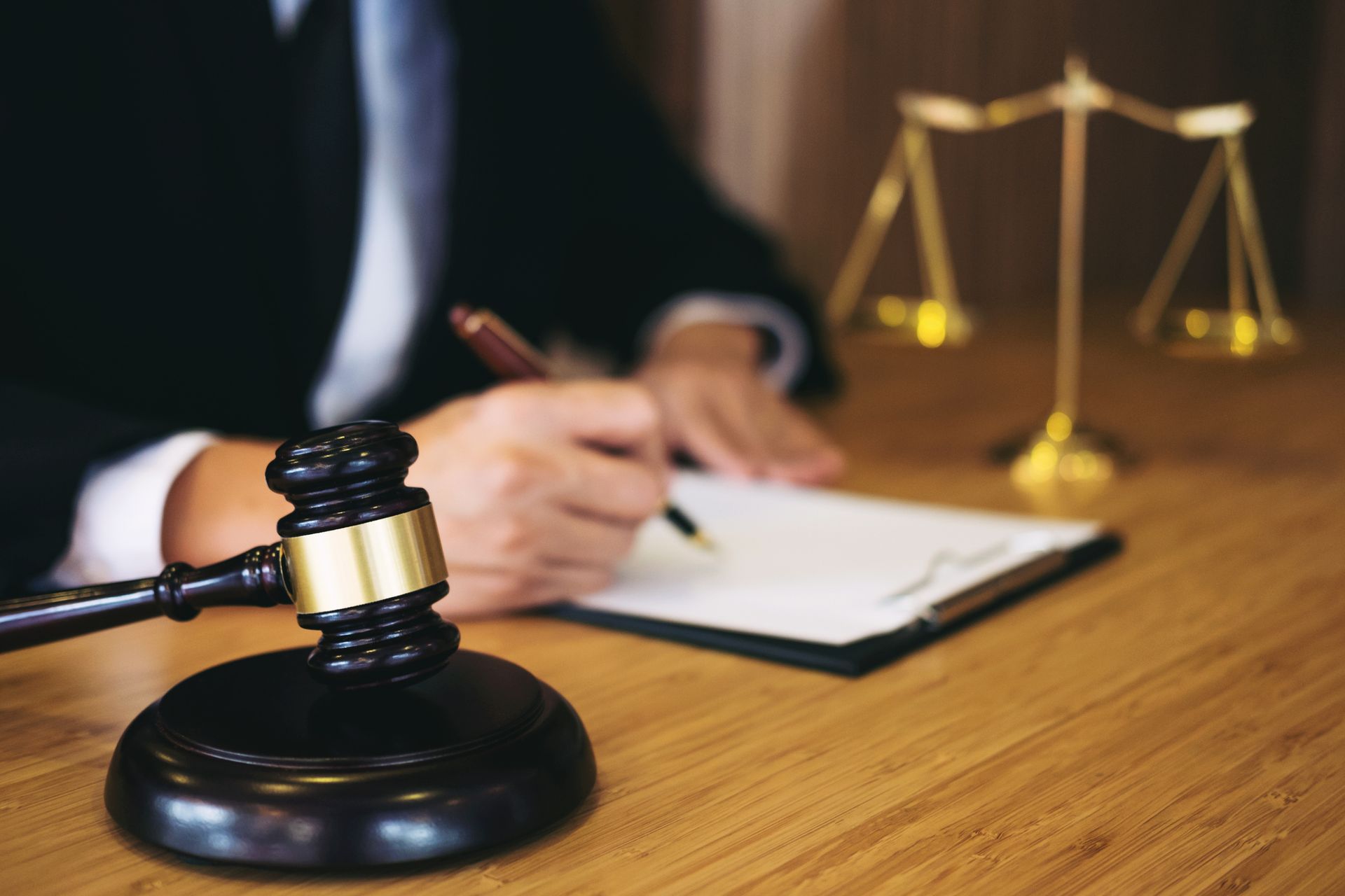 Attorney signing legal documents at desk with judge's gavel and scales of justice.
