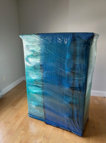 Blue plastic-wrapped rectangular object standing on a hardwood floor in a bare room