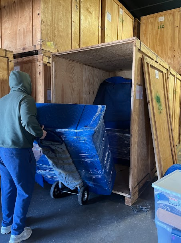 Person pushing a blue cart into a wooden storage bay in a warehouse