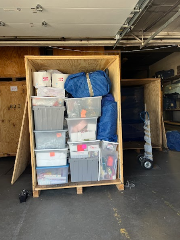 Storage cabinet packed with plastic bins, buckets, and blue bags in a garage or warehouse.