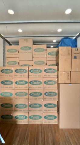 Stacks of cardboard boxes packed in a truck or storage area, with wood flooring and overhead lights.