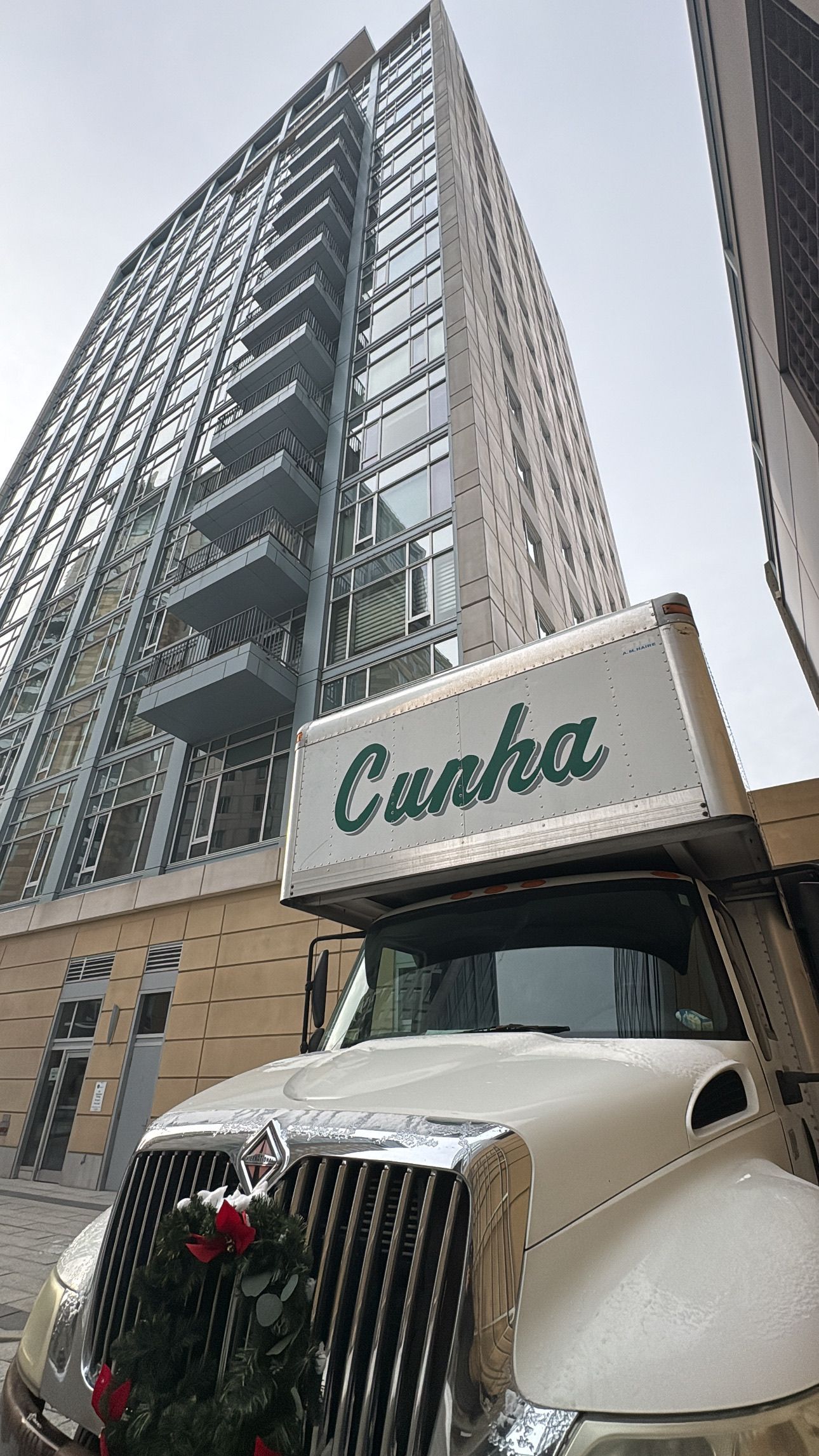 Tall city building behind a cream Curb truck with a chrome grille and holiday wreath on the front