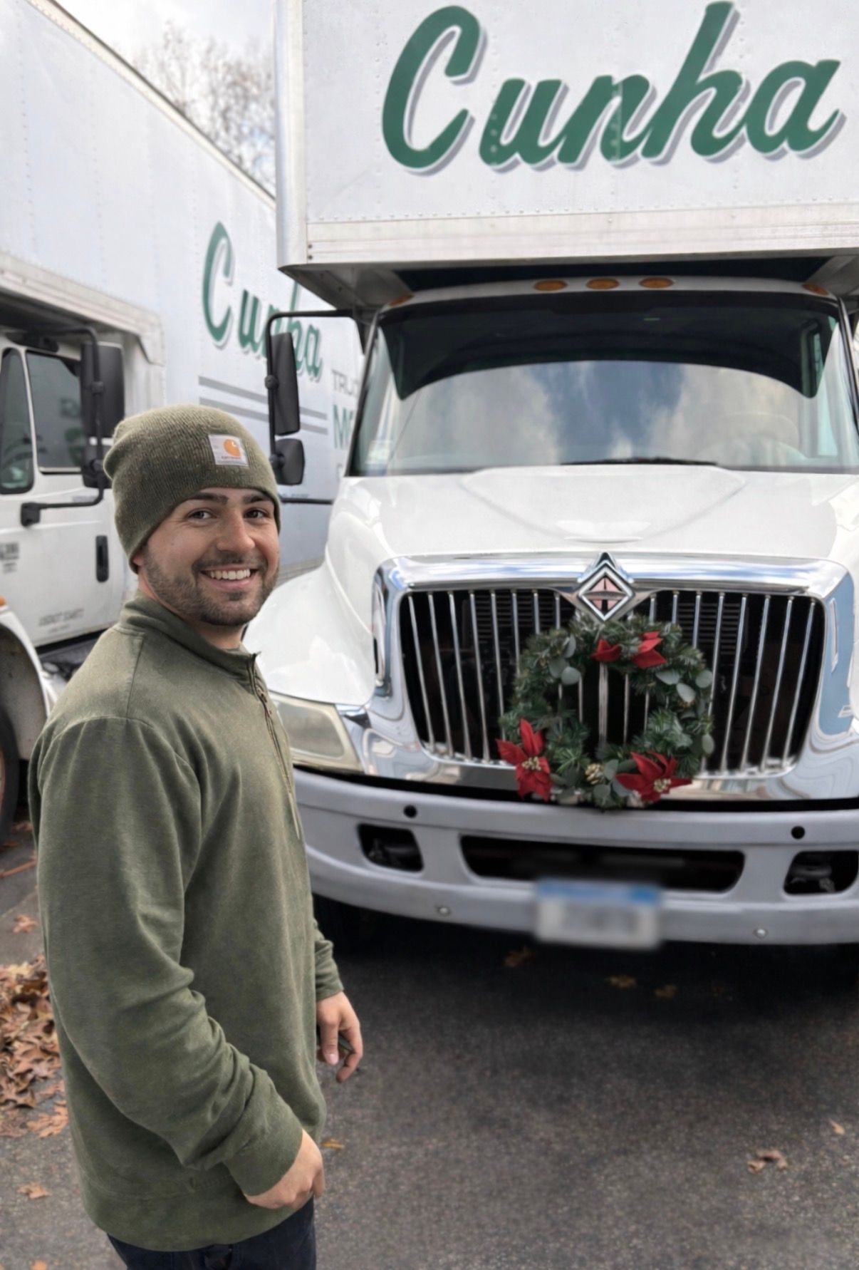 Smiling man in green sweater standing by a white Cupha truck decorated with a holiday wreath.