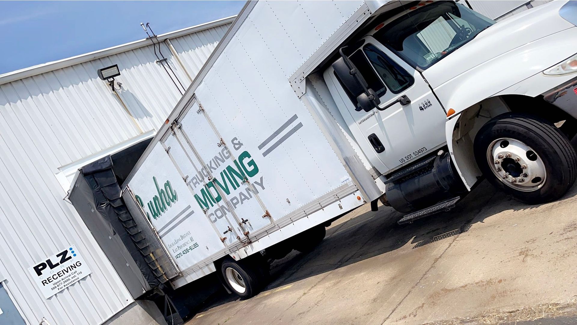 White Moving truck parked outside a warehouse at an angle, with a box truck and trailer visible.