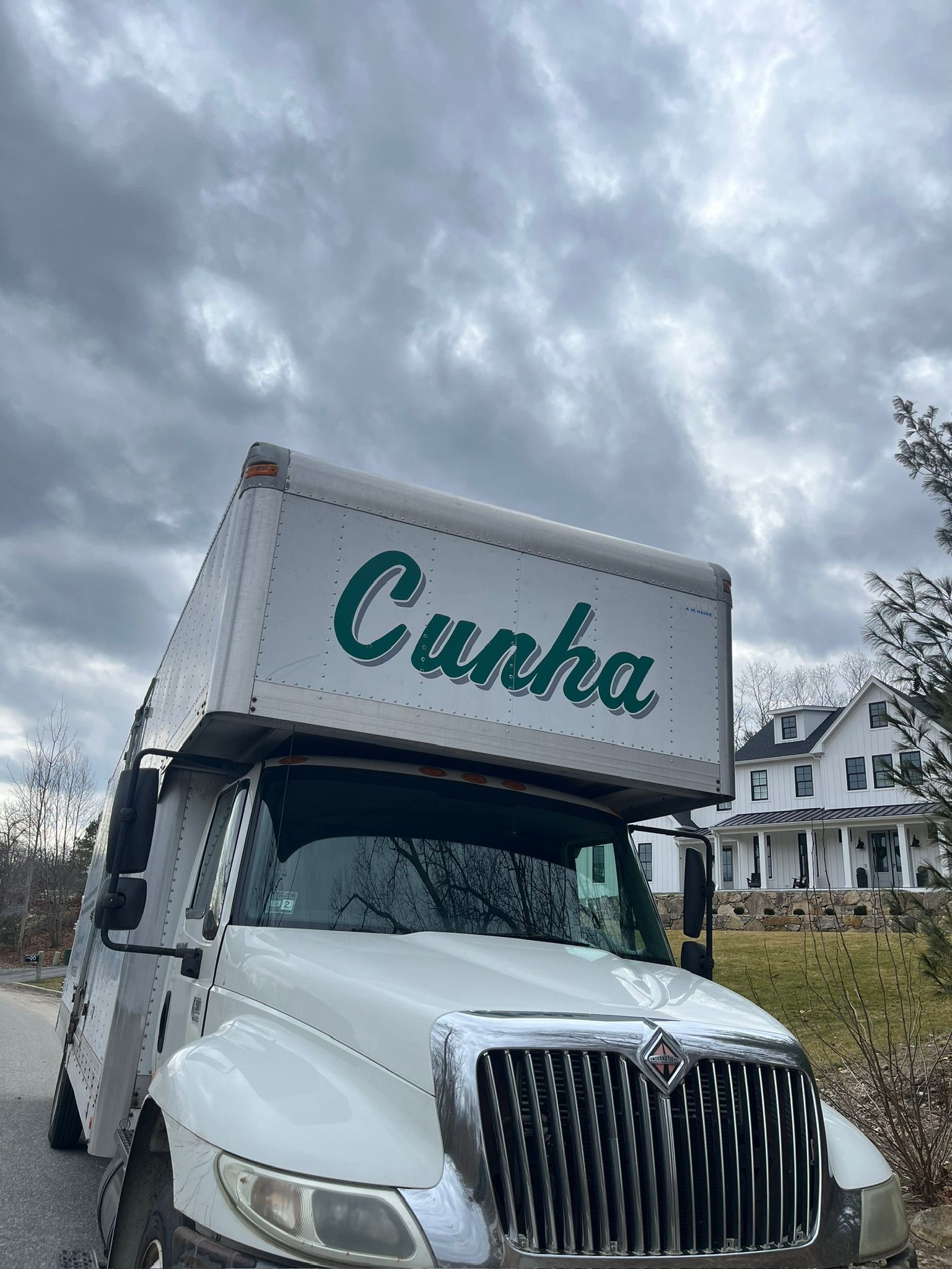White box truck with “Cuaha” on the cab driving under a cloudy sky.