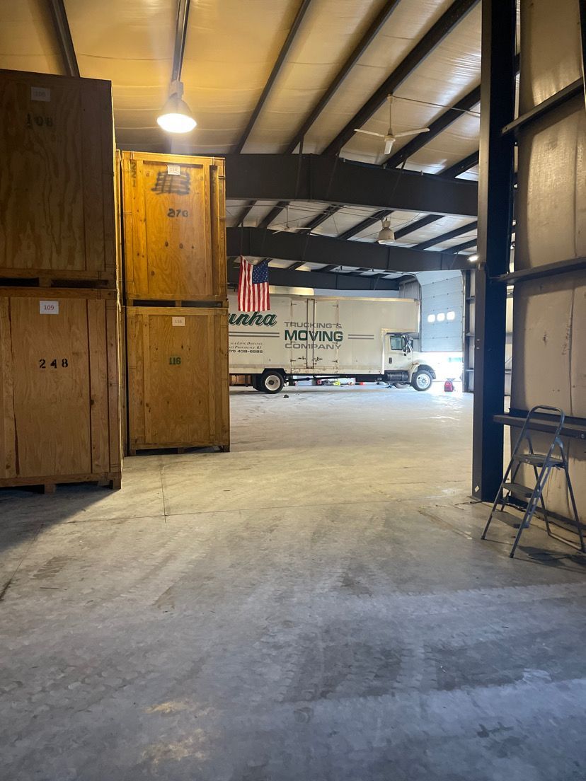 Warehouse interior with stacked wooden crates and a truck visible through an open doorway.