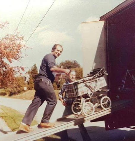 Man loading a plaid-covered baby stroller up a truck ramp outdoors