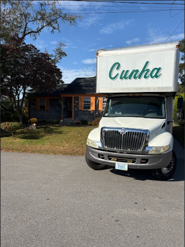 White Cunha moving truck parked on a street in front of a house on a sunny day