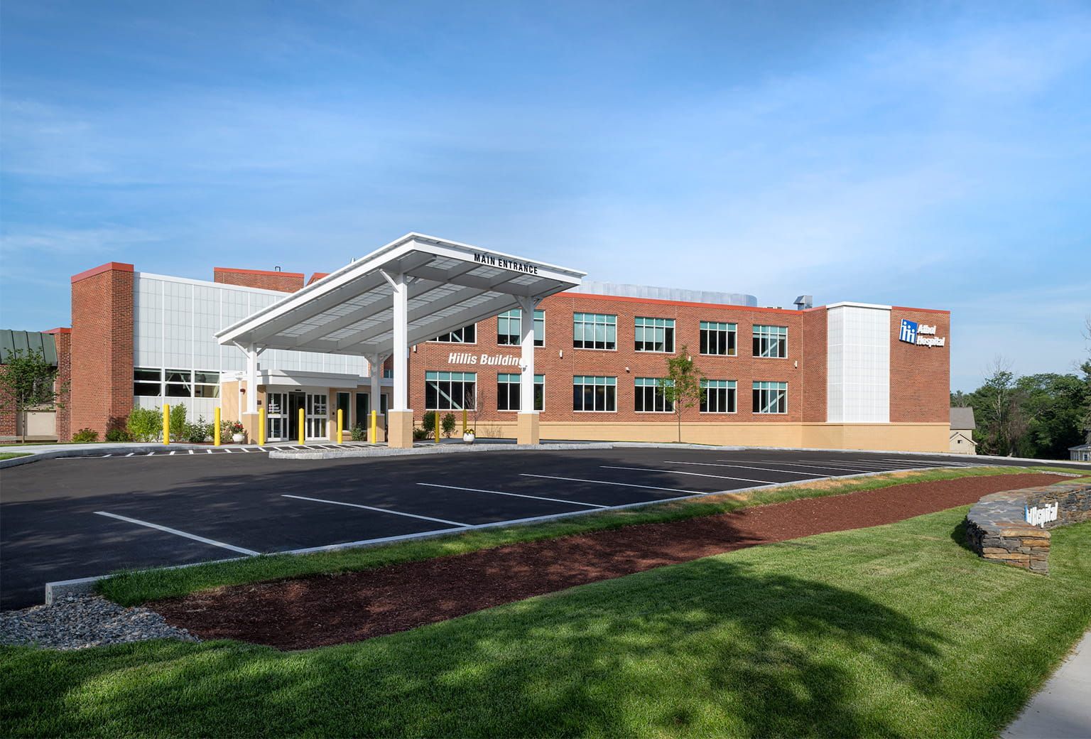 Modern brick building with a white canopy entrance and empty parking lot under a blue sky