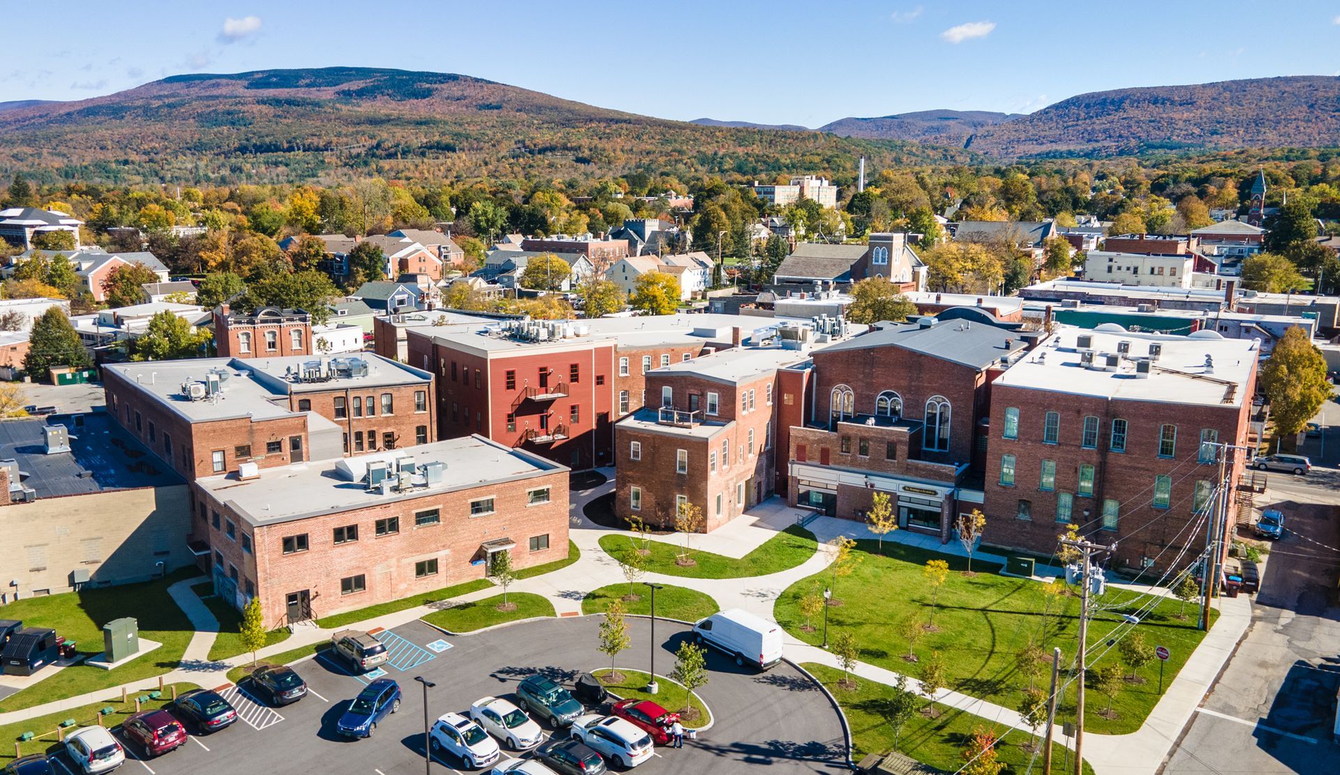 Aerial view of a brick campus building with parking lot, trees, and hills in the background
