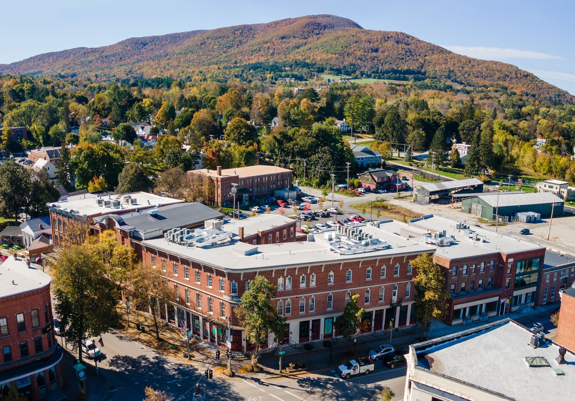 Aerial view of a small town with red-brick buildings, trees, and a mountain in the background