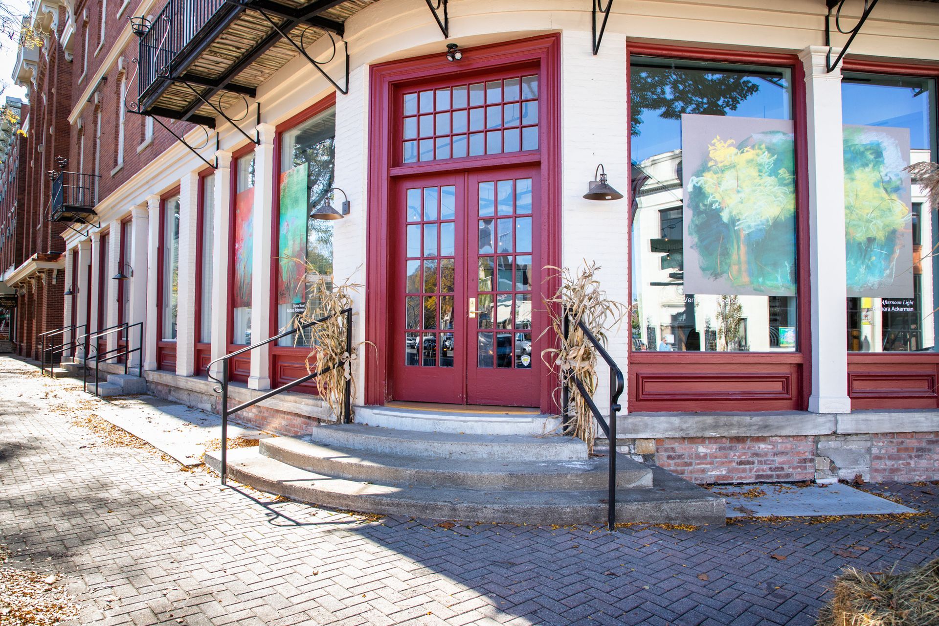 Sunlit brick storefronts with red-trimmed windows and a sidewalk cafe on a cobblestone street