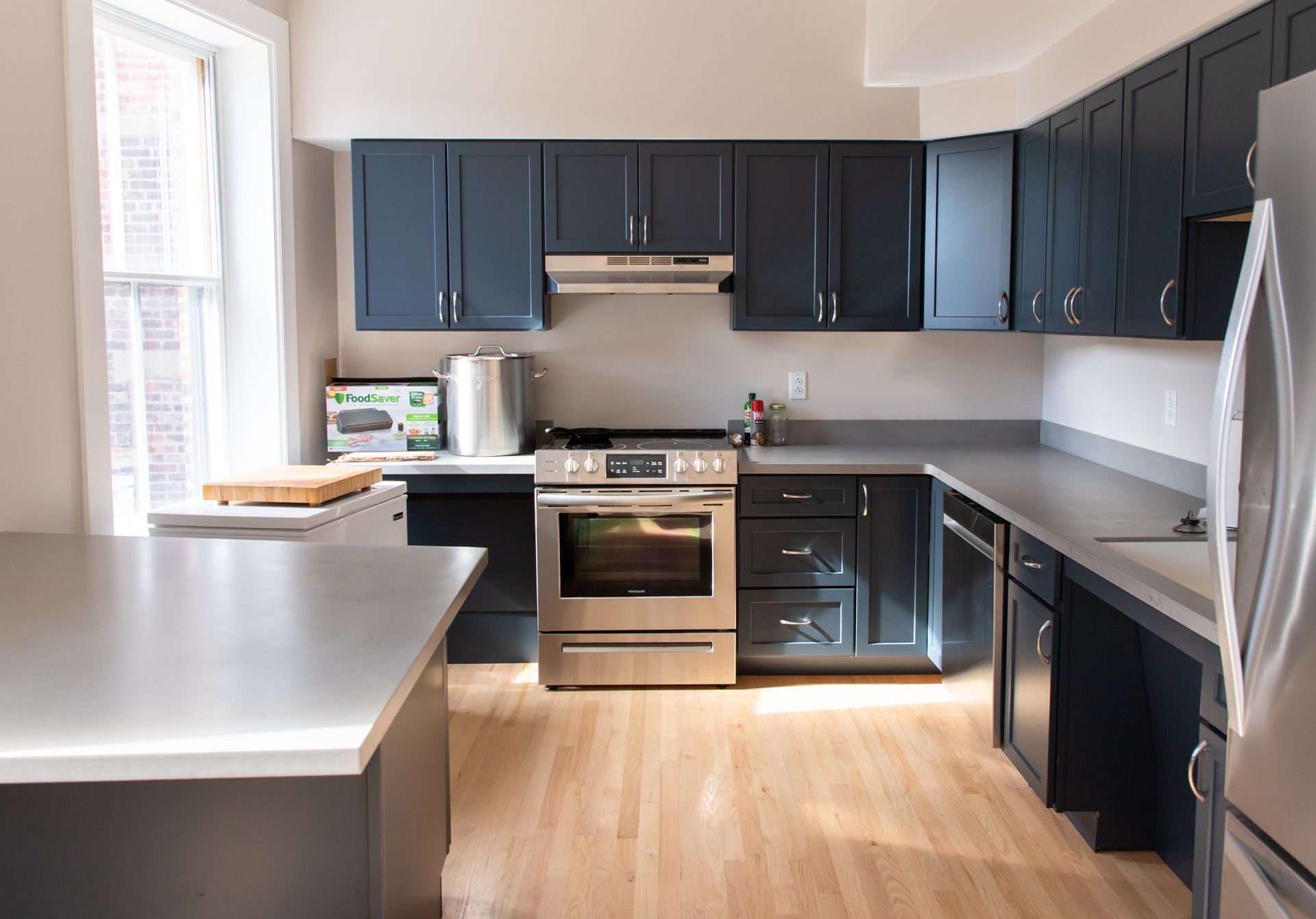 Modern kitchen with dark cabinets, stainless steel appliances, and a light wood floor.