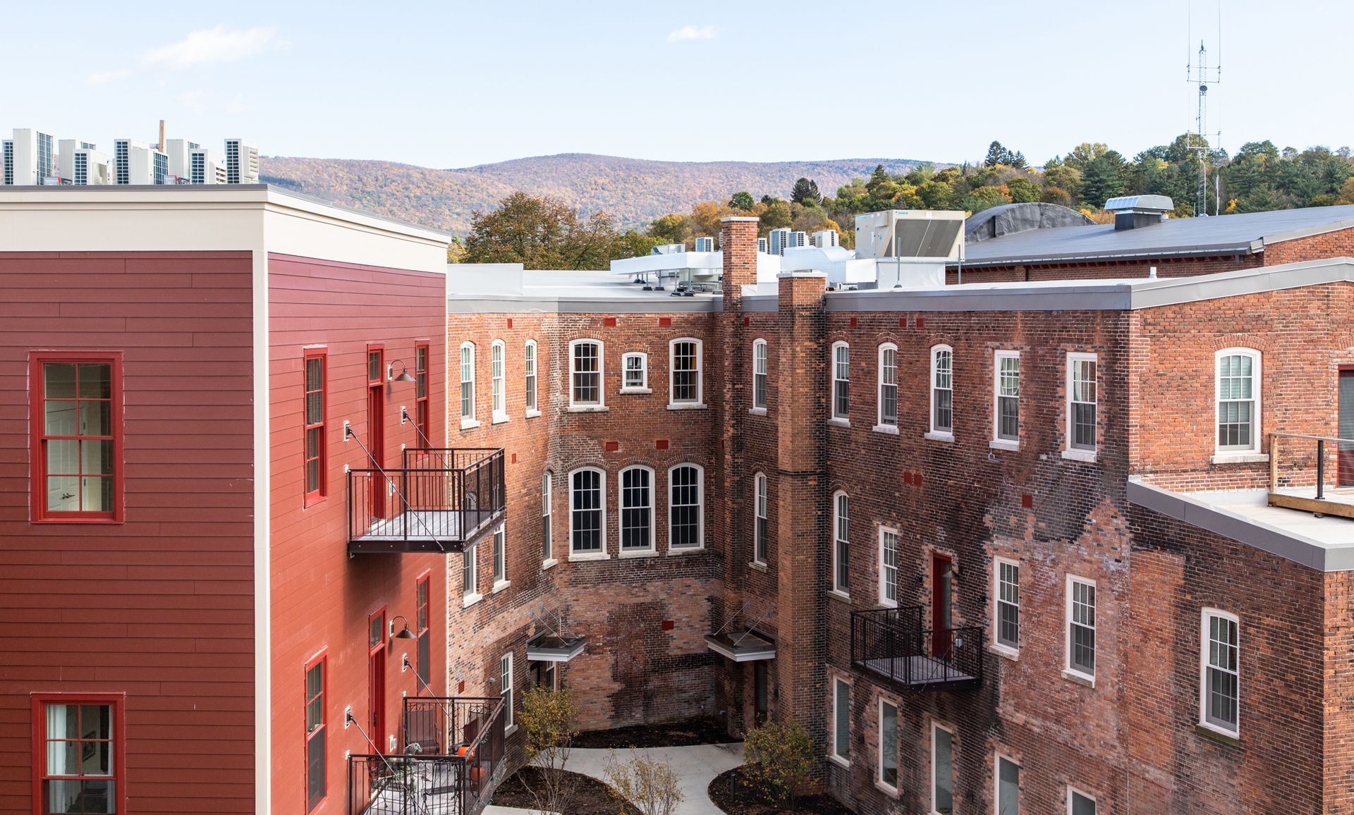 Red brick apartment buildings with balconies and rooftops, viewed across a narrow courtyard under a clear sky