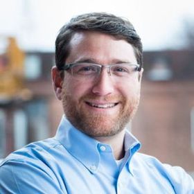 Smiling man in glasses and a blue shirt in a bright indoor setting