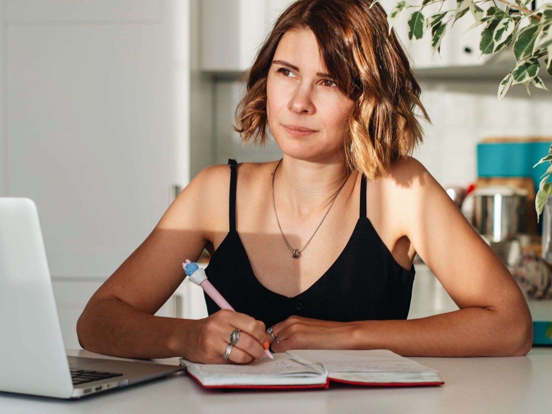 A woman is sitting at a table with a laptop and a notebook.
