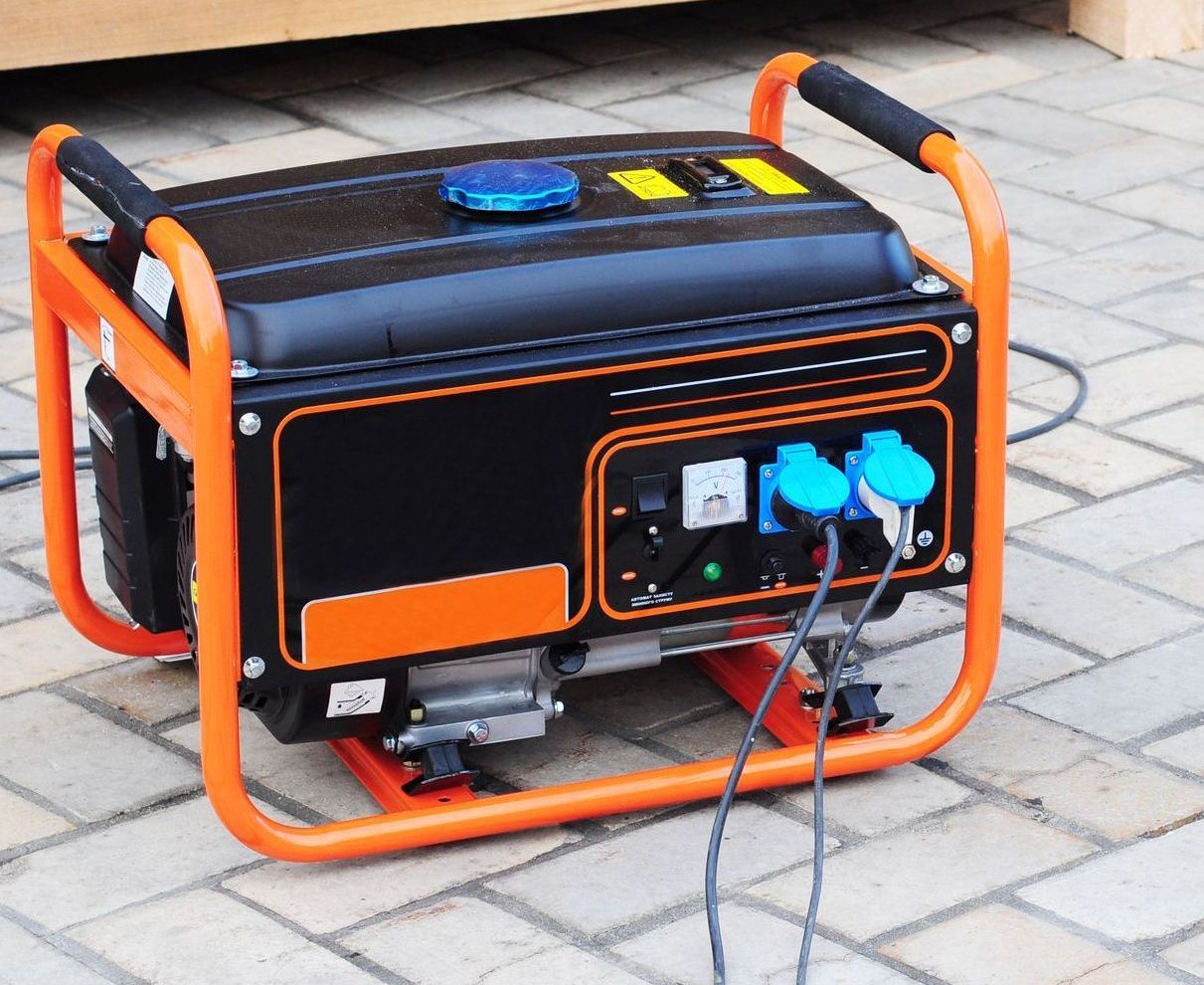 A black and orange generator is sitting on a brick sidewalk.